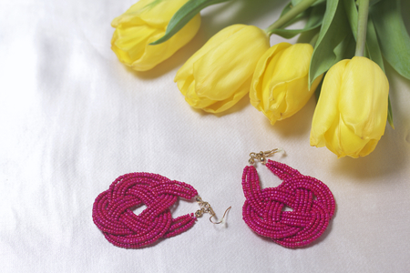 Gifts for loved ones. A bouquet of yellow tulips is scattered on a light surface. Nearby are handmade earrings.の写真素材