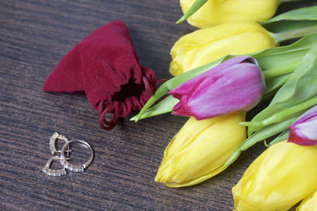 Gifts for loved ones. A bouquet of yellow and pink tulips is scattered on a dark surface. Nearby is an open velvet bag of red color with gold jewelry.の写真素材