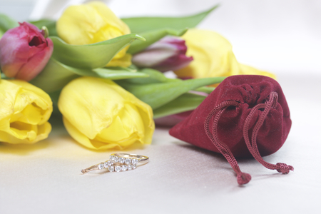 Gifts for loved ones. A bouquet of yellow and pink tulips is scattered on a light surface. Nearby is an open velvet bag of red color with gold jewelry.の写真素材