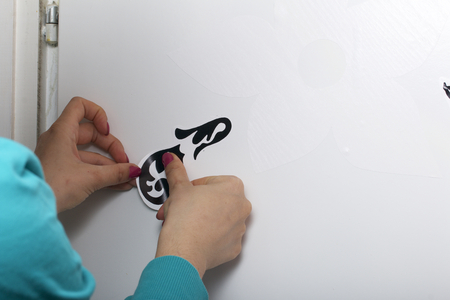 The girl glues the cut out elements from self-adhesive paper, to mask the defects of the white door.の写真素材