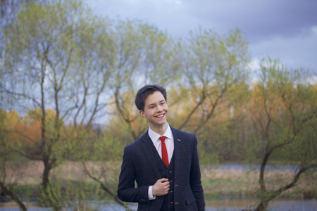 A young man, a teenager, in a classic suit. Walking along the avenues of the spring park.の写真素材