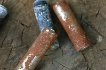 Spent batteries, coated with corrosion. Different shapes and sizes. lie on the edge of a wooden...