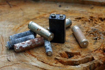Spent batteries, coated with corrosion. Different shapes and sizes. lie on the edge of a wooden...