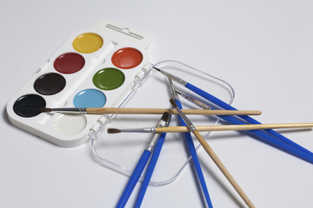Watercolors and brushes on a white surface. Next glass for water. Subjects for creativity.の写真素材