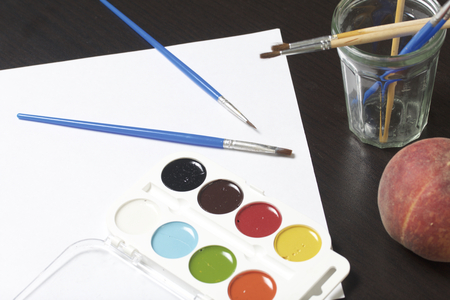 Watercolors and brushes on a dark surface. Nearby is a peach for a still life. Subjects for creativity.の写真素材