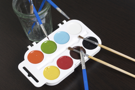 Watercolors and brushes on a dark surface. Nearby is a glass for water. Subjects for creativity.の写真素材