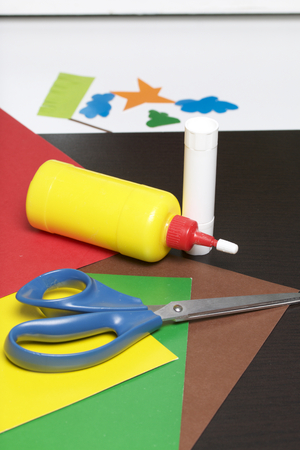 Lessons in applique. Necessary items: glue, colored paper and scissors lie on the dark surface of the table. Cut several elements.の写真素材