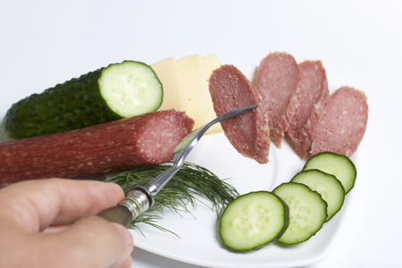 The man makes an easy snack. On the saucer are sausage, cucumber, tomato, cheese and dill.の写真素材