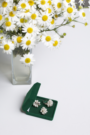 An open green velvet box for jewelry. In it lies a set: a ring and earrings with pearls. Next to the vase is a bouquet of chamomile. On a white background.の写真素材