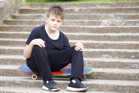 A teenager with a skateboard. Sits on a skateboard against the backdrop of a stone staircase.の写真素材