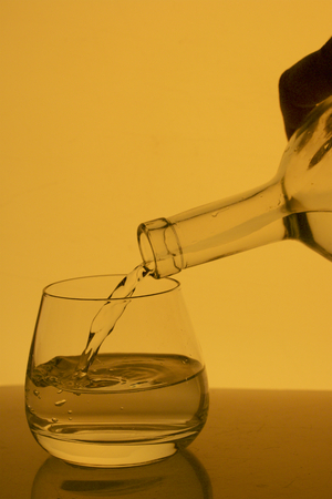 Alcoholic beverage in a glass goblet. A drink is poured into it from the bottle.の写真素材