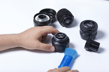 The man is brushing the dust off the lens of the lens with a brush. Nearby on the table are other vintage lenses.の写真素材