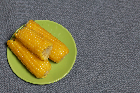 The cob of boiled corn lies on a saucer. Against the background of sacking.