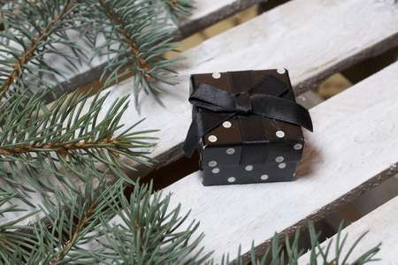 Blue spruce branches on a wooden box of boards, painted in white. Nearby is a black gift box with a bow.の写真素材
