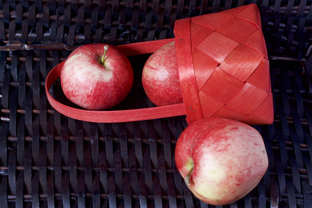 Ripe aromatic apples in a red wicker basket. Against the background of a wicker basket of wicker.の写真素材
