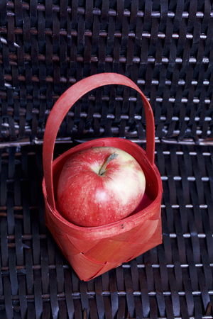 Ripe aromatic apples in a red wicker basket. Against the background of a wicker basket of wicker.の写真素材