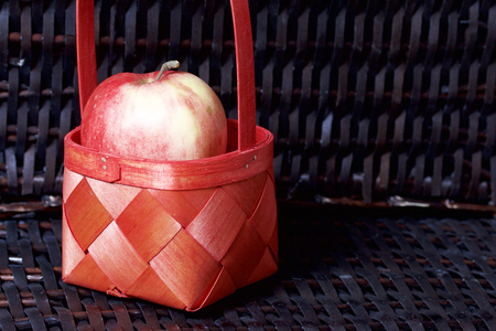 Ripe aromatic apples in a red wicker basket. Against the background of a wicker basket of wicker.の写真素材