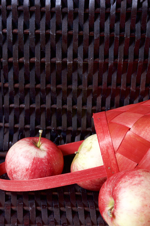 Ripe aromatic apples in a red wicker basket. Against the background of a wicker basket of wicker.の写真素材