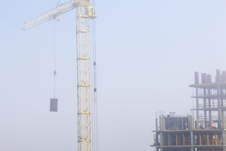 Tower cranes on the construction of a building with a frame of reinforced concrete. Works in the morning mist.の写真素材