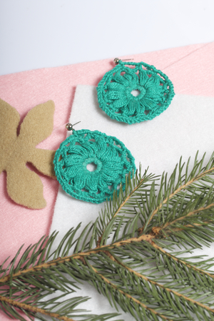 Knitted earrings on the background of felt fabric. Near spruce branch.