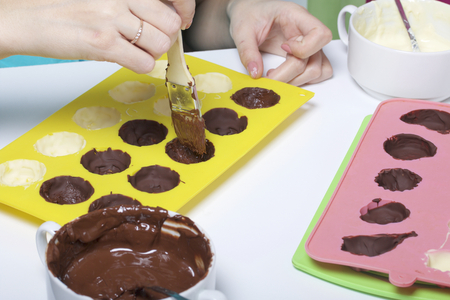 A woman using a brush brushes a silicone dessert mold with a melted black chocolate. Nearby are other ingredients.の写真素材