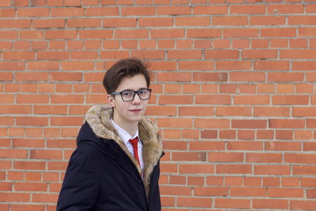 Portrait of a young man in a coat with a fur collar. On the background of a brick wall.の写真素材