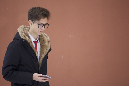 Portrait of a young man in a coat with a fur collar. Holds a smartphone in his hand.の写真素材
