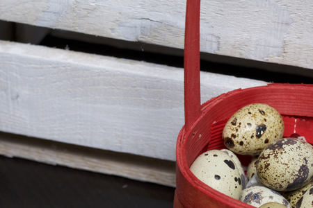 Quail eggs. They lie in a red wicker basket next to a wooden box.の写真素材