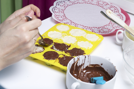 A woman smears chocolate filling coconut and condensed milk. Ingredients for dessert are on the table. Cooking sweets with coconut and condensed milk. In a glaze of white and black chocolate.の写真素材