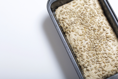 Baking bread at home. Wholemeal dough lies in bread pan. Sunflower seeds are scattered on the surface of the dough.の写真素材