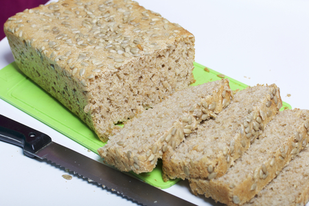 Baking bread at home. A loaf of freshly baked wholegrain bread with sunflower seeds lies on a cutting board. Bread slices and a knife are visible.の写真素材