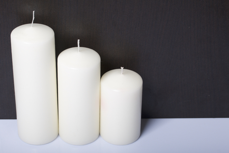 Candles white in different sizes. White background turning into dark.の写真素材