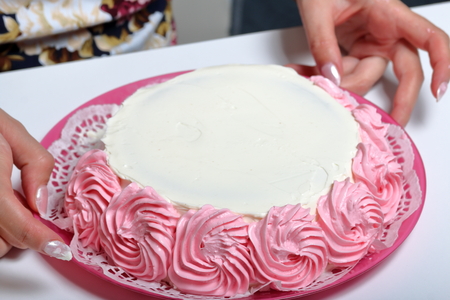A woman holds in her hands an unfinished cake, decorated with a cream of pink color.の写真素材