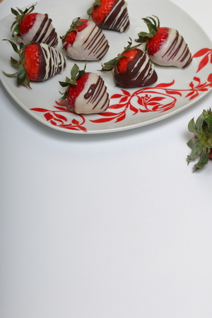 Strawberries glazed in black and white chocolate. Lie on a white plate with a pattern.の写真素材