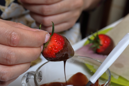 A woman dips strawberries in black melted chocolate. Cooking strawberries glazed in chocolate.の写真素材