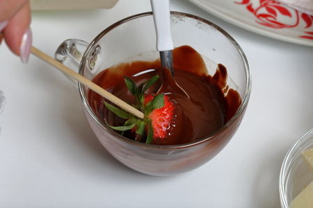 A woman dips strawberries in black melted chocolate. Cooking strawberries glazed in chocolate.の写真素材
