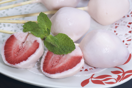 Strawberries in yogurt. Berries are dressed on wooden skewers and dipped in yogurt. Nearby are two halves of dessert. Visible red juicy strawberry flesh. Decorated with mint leaves.の写真素材