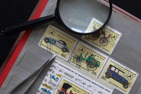 Postage stamps of the Republic of Korea in the album. Released to the 60th anniversary of Mercedes-Benz (1926-1986). Depicted various cars model range. Next magnifying glass and tweezers.のeditorial素材