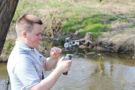 A young man videotaping on a smartphone. Uses gimbal to get smooth footage. Closely watching the movie shooting.の写真素材
