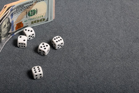 White dice with black markings. They lie on a surface covered with a coarse gray cloth. Nearby are a few dollar bills of different denominations.の写真素材