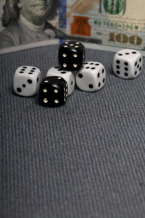 White and black dice with black markings. They lie on a surface covered with a coarse gray cloth. Among them are two black dice with white markings. Nearby is a hundred dollar bill.の写真素材