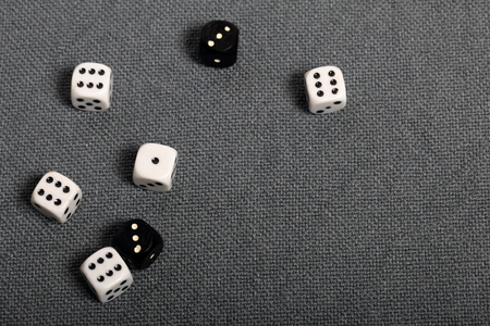 White and black dice with black markings. They lie on a surface covered with a coarse gray cloth. Among them are two black dice with white markings.の写真素材