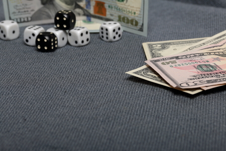 White and black  dice with black markings. They lie on a surface covered with a coarse gray cloth. Among them are two black dice with white markings. Nearby are a few dollar bills of different denominations.の写真素材