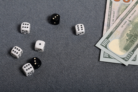 White and black dice with black markings. They lie on a surface covered with a coarse gray cloth. Among them are two black dice with white markings. Nearby are two hundred dollar bills.の写真素材