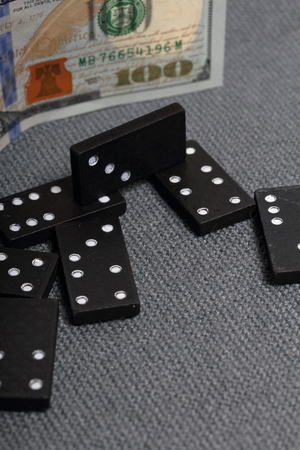 Domino knuckles on a surface covered with a coarse gray cloth. Nearby is a hundred dollar bill.