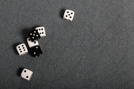 White and black dice with black markings. They lie on a surface covered with a coarse gray cloth. Among them are two black dice with white markings.の写真素材
