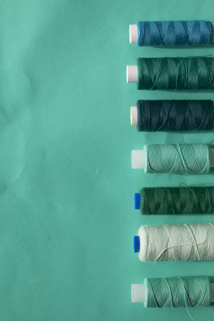 Spools of different colors are arranged in a row on a turquoise background. In the style of flat...