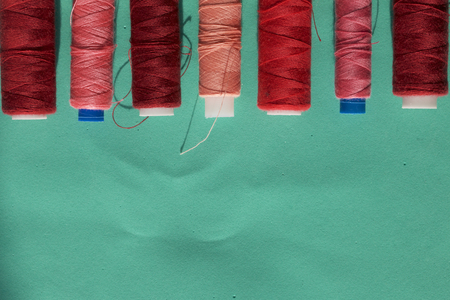 Spools of different colors are arranged in a row on a turquoise background. In the style of flat...