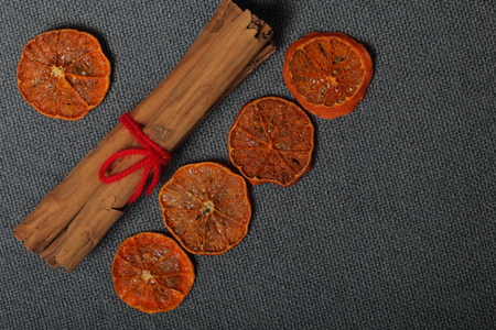 Tangerines are cut into slices and dried to decorate desserts. Nearby are cinnamon sticks tied with red thread. On a gray background.の写真素材