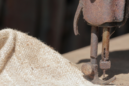 Old sewing machine, with manual drive. Covered with corrosion, dust and cobwebs. A piece of coarse fabric is sewn into it.の写真素材